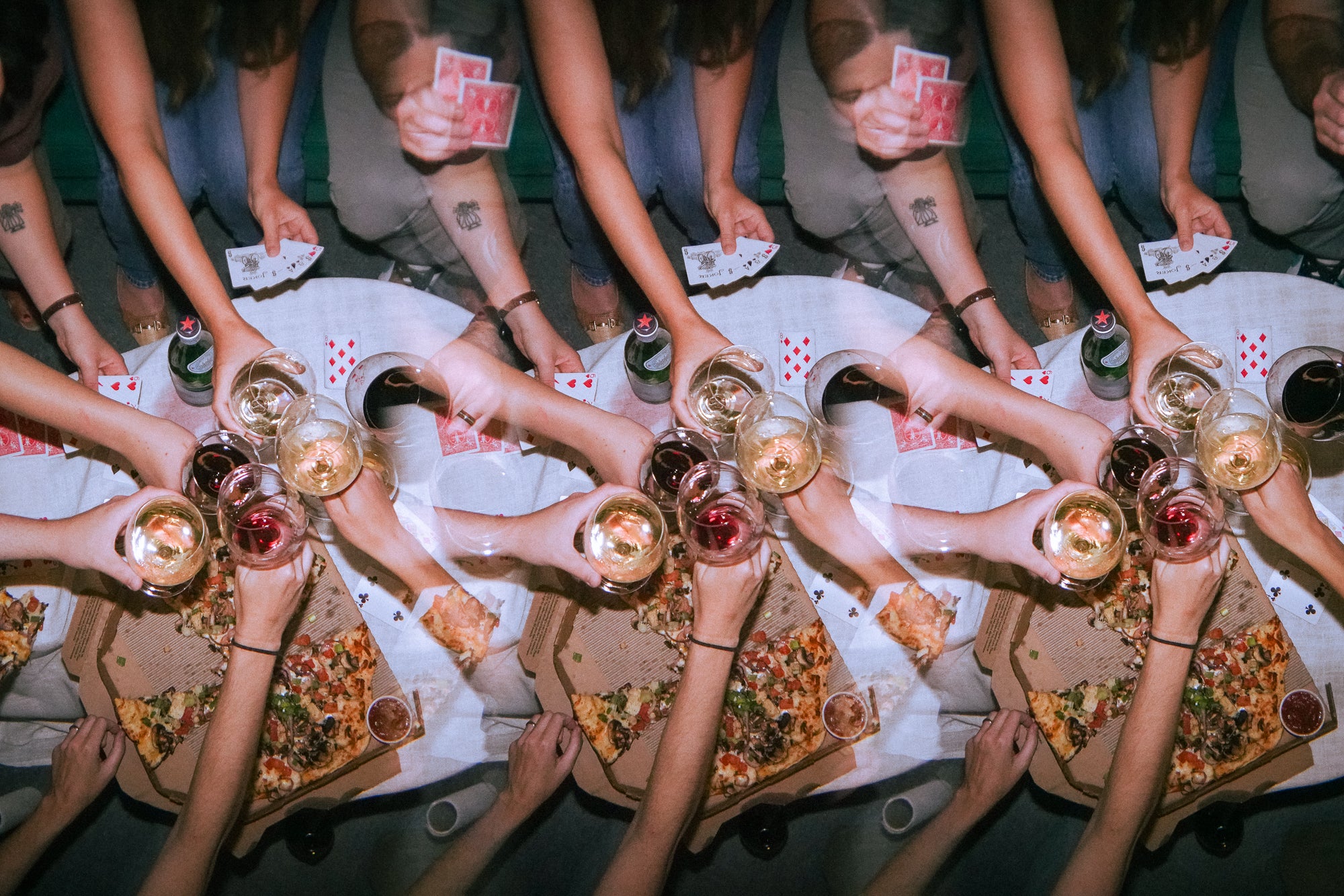 A group clinks glasses over a pizza party with playing cards, representing the luck of the draw.